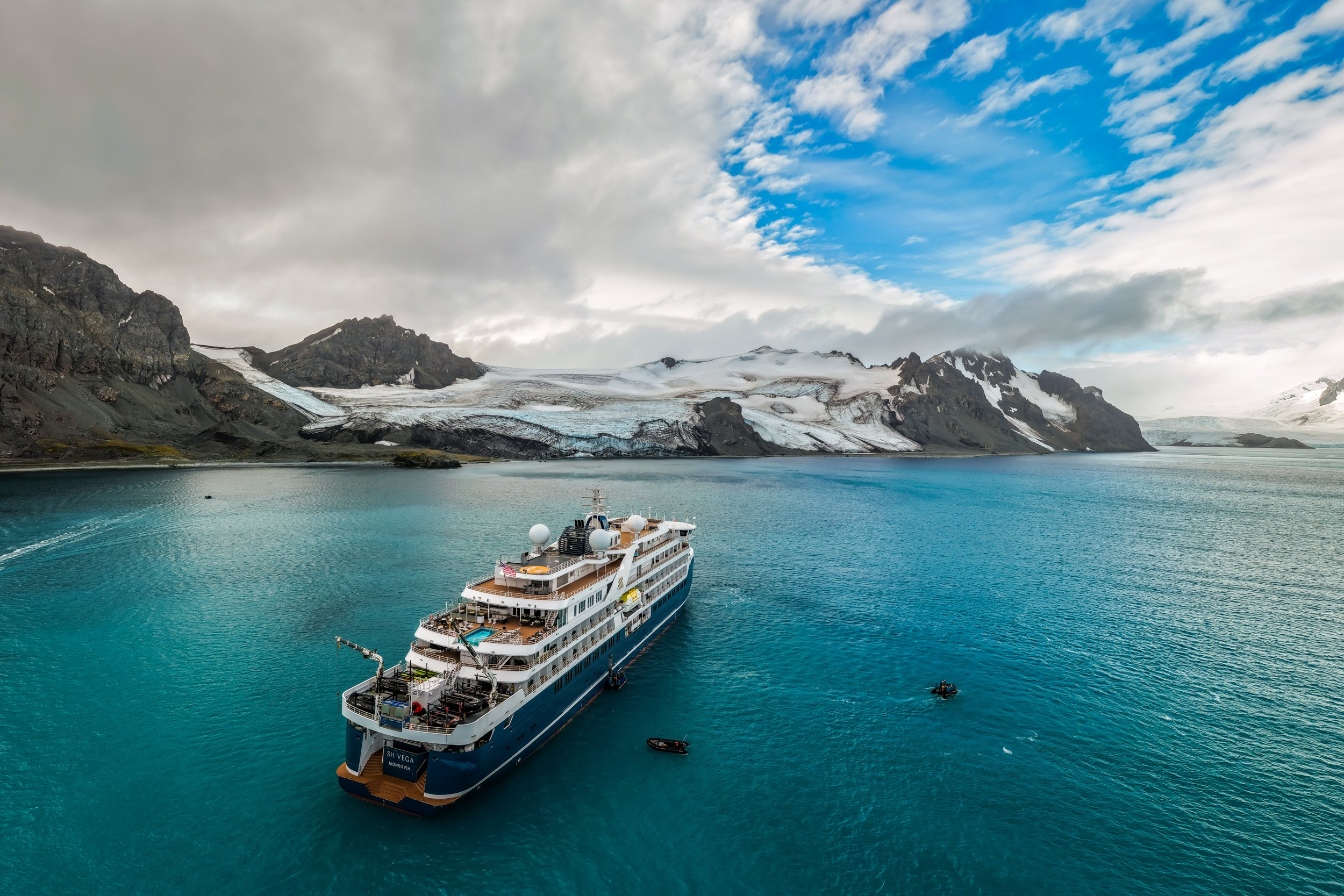 Paisagem antártica com montanhas nevadas, icebergs e colônia de pinguins ao longe
